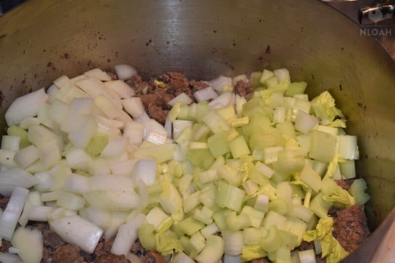 chopped celery and onions over ground beef in metal bowl