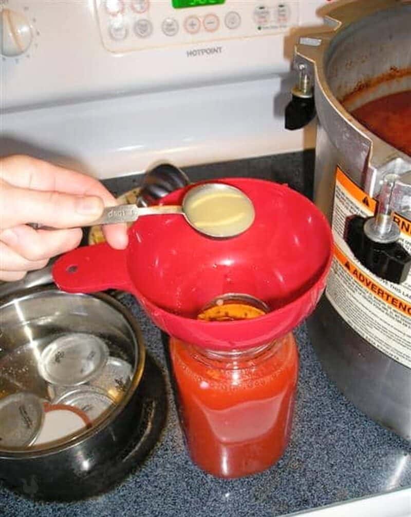 adding lemon juice to jar full of tomato juice to can