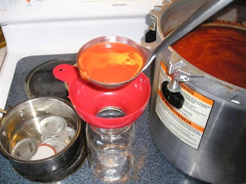 ladling hot tomato juice into canning jar