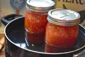 two jars filled with cooked tomatoes in hot water bath