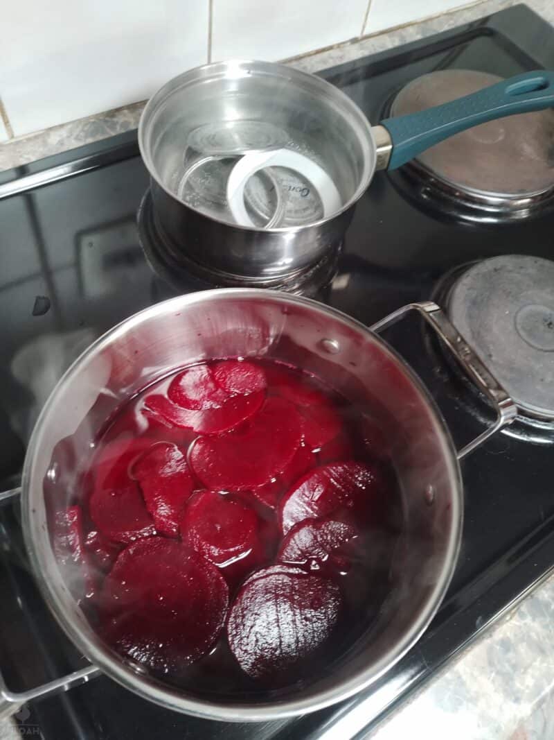sliced beets boiling on stovetop next to pot with canning lids