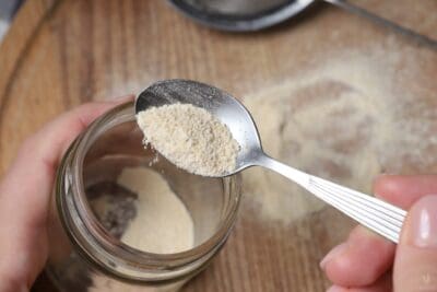 adding garlic powder to glass jar with spoon