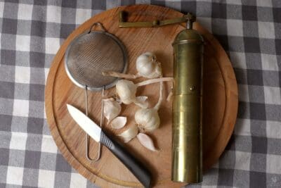 garlic on cutting board next to knife and grinder