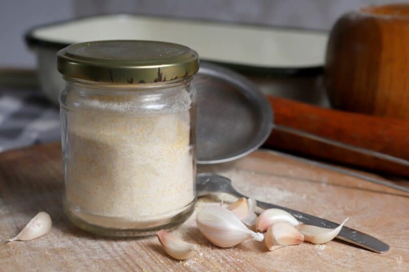 garlic powder in jar next to garlic cloves