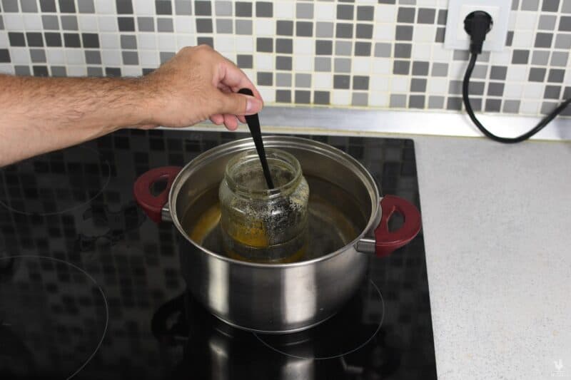 stirring crystallized honey inside jar in boiling water