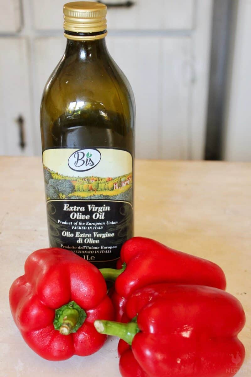 three red bell peppers next to bottle of olive oil