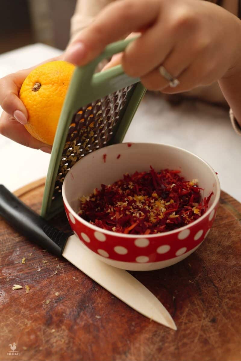 grating an orange over carrot and beetroot